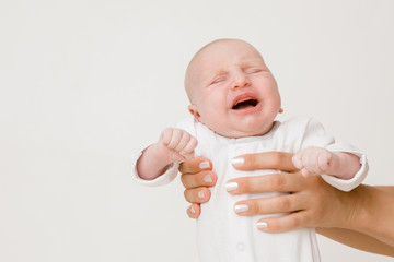 Mother hands holding crying infant on gray background. Close up. Month old baby girl.