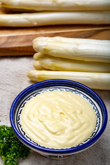 Bunch of fresh uncooked white asparagus and hollandaise sauce in bowl