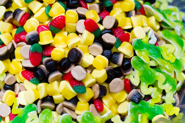 a scattering of marmalade sweets of different colors, mainly in the form of cakes and berries with edible frogs along the edges.