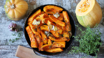 Baked pumpkin slices in a pan with herbs and garlic. Autumn lunch. Vegan food. Healthy snack.