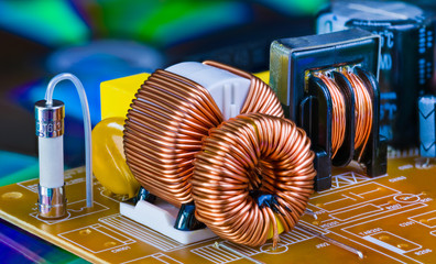 Toroidal inductors with copper wire winding, transformer and electric fuse. Electronic components on circuit board detail from dismantled power supply unit. Induction coils on blue colored background. - obrazy, fototapety, plakaty