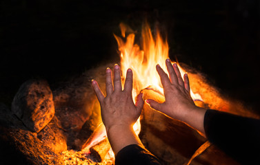 Blazing bonfire and old lonely woman in detail on night black background. Female hands with fingers...