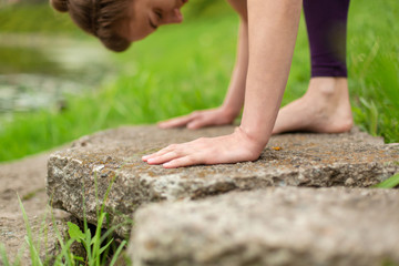 A young sports girl practices yoga in a quiet location on the river bank in summer, in a yoga asana pose. Meditation and oneness with nature