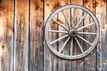 A wooden wheel with a metal hoop hangs on a wall made of old wooden planks.