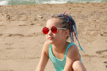 cute girl in fashionable red glasses and colored pigtails sitting on the beach - Powered by Adobe