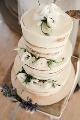 Wedding ceremony. Beautiful pie on the table. Elegant wedding cake decorated with white eustoma and vanilla glaze with bride and groom on background. Brides cut cake together. Close up