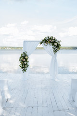 Wedding decor. White wedding arch stands on the shore of a lake or river. Decorated with flowers.