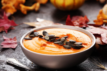 Roasted pumpkin and carrot soup with cream and pumpkin seeds on wooden background.