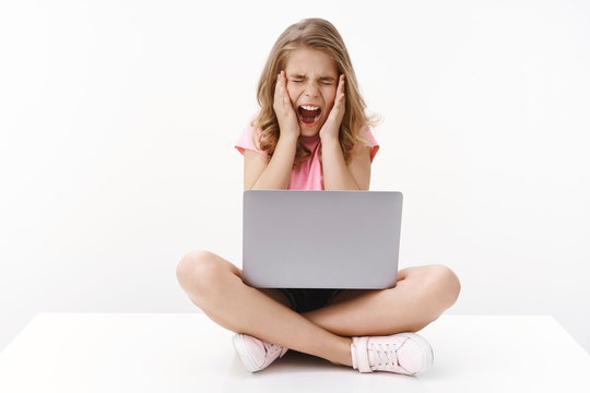 Scared terrified young cute caucasian blond girl scream from fear, sit crossed legs hold laptop, close eyes and shouting shocked frightened, touch face terrified, pose white background