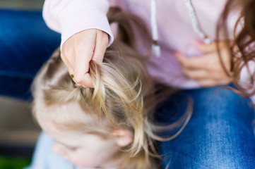 Weaving braids for a child. Hands of a woman who weaves a braid from the hair of a blonde girl, close up