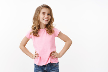 Boastful confident good-looking blond little girl, hold hands on waist self-assured, smiling...