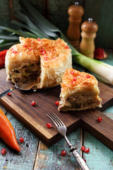 Savory phyllo pastry pie with chicken and vegetables decorated with pomegranate seeds on dark oak board