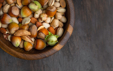 Various nuts in wooden bowls on dark wooden background . Almonds , pistachios, hazelnut and pumpkin seeds Top view