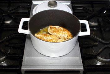 Delicious braised chicken breast cooked in a Dutch oven resting on the stove top in a home kitchen.