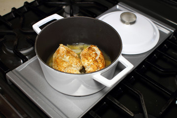 Delicious braised chicken breast cooked in a Dutch oven resting on the stove top in a home kitchen.