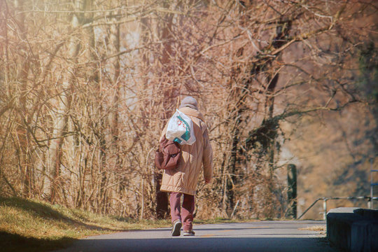 beggar old woman, poverty concept - a tramp lady walking alone on the street (back view)