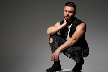 Tough young man touching his neck and squatting