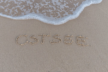 Schriftzug Ostsee im Sand mit Welle - 294244095
