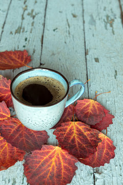 Turquoise cup of coffee and red autumn leaves on a vintage wooden background with peeling paint.