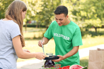 Young volunteer giving food for poor woman outdoors