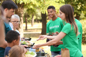 Young volunteers giving food to poor people outdoors
