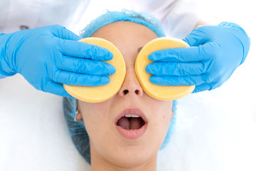Naklejka premium A woman, a professional doctor, a beautician cleanses the patient's face with sponges before applying the mask for skin care