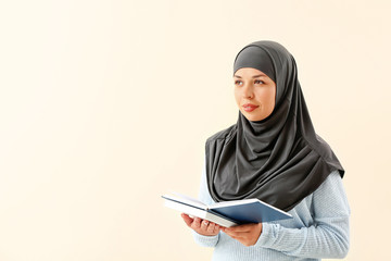 Portrait of Muslim woman with books on light background