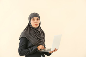 Portrait of Muslim woman with laptop on light background