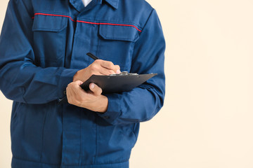 Male car mechanic with clipboard on color background