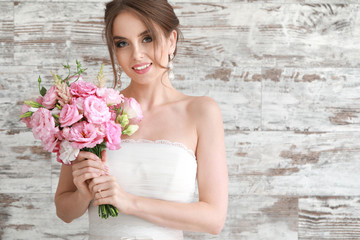 Portrait of beautiful young bride with wedding bouquet on wooden background