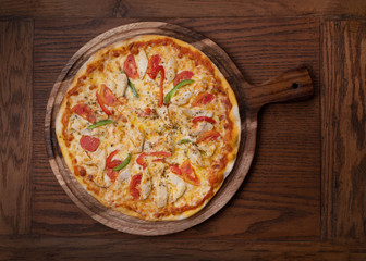 Top view of fresh tasty pizza with chicken, tomato, paprika and mozzarella cheese on wooden...
