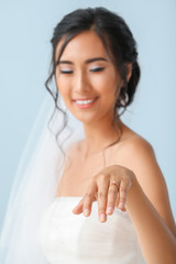 Beautiful young Asian bride showing her wedding ring against color background