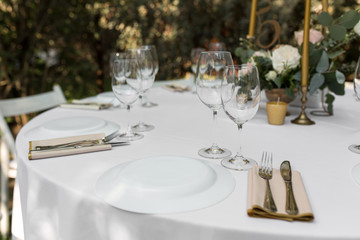 Fototapeta na wymiar Wedding table setting decorated with fresh flowers in a brass vase. Wedding floristry. Banquet table for guests outdoors with a view of green nature. Bouquet with roses, eustoma and eucalyptus leaves