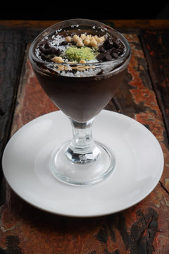 Chocolate mousse pudding with coconut, pistachio powder and chocolate chips isolated on rustic wooden table. Supangle or sup is a type of Turkish chocolate pudding