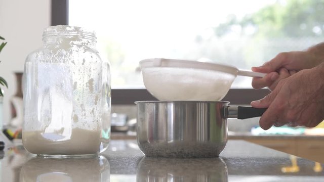 Daily preparation of milk kefir in the kitchen. A man puts kefir in a mesh strainer to separate the milk kefir grains from finished kefir to have a health probiotic aliment. A superfood
