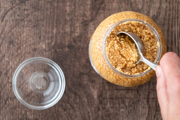 Glass jar of minced garlic and small glass bowl on wood background, woman’s hand using tablespoon to scoop out garlic