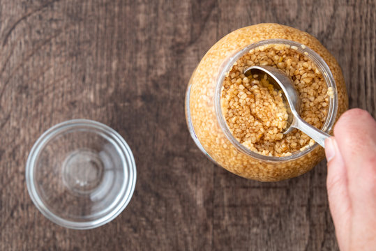 Glass jar of minced garlic and small glass bowl on wood background, woman&rsquo;s hand using tablespoon to scoop out garlic