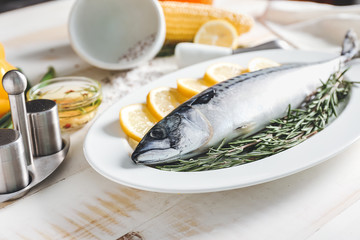 Plate with raw mackerel fish, lemon and rosemary on wooden table