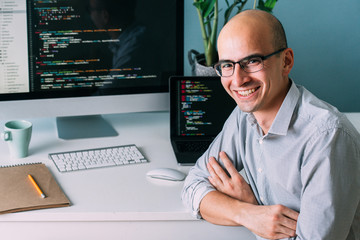 Programmer, working behind the desk, with two screens filled with code lines