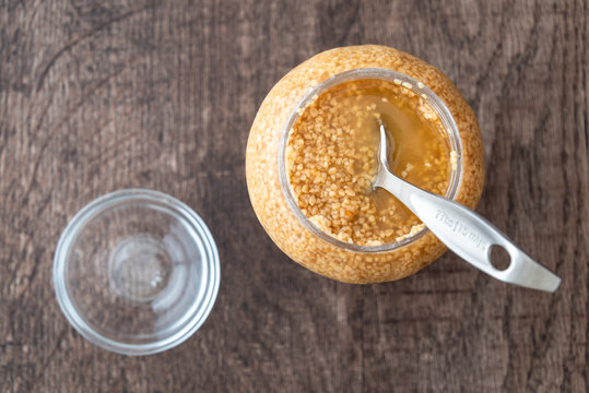 Glass jar of minced garlic and small glass bowl on wood background, with stainless steel tablespoon in jar