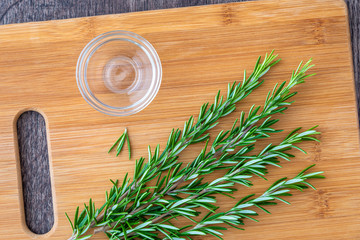 Fresh sprigs of rosemary with on a bamboo cutting board, small glass bowl