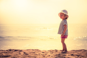 Child standing alone on beach with bright orange sunset sunlight during summer beach holidays concept happy childhood travel lifestyle 