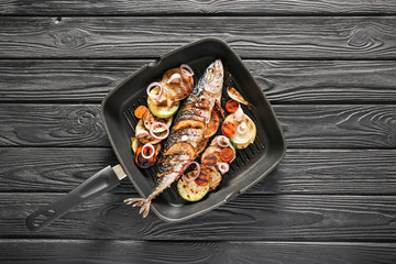 Grill pan with prepared mackerel fish and vegetables on dark table