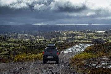 Off-road car on the stoned road in the tundra at rain weather