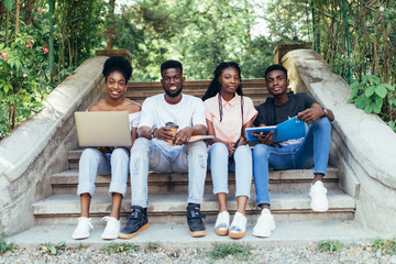 Emotional african students looking excited in laptop, sitting outside on campus stairs, education.
