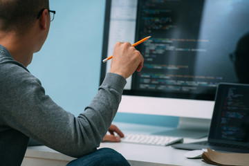 Programmer, working behind the desk, analysing code on the black screen.