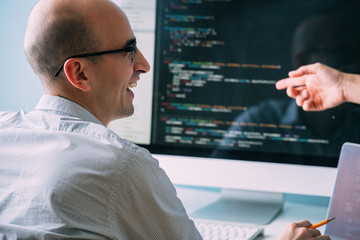 Programmer, working behind the desk, analysing code while chatting with coworker