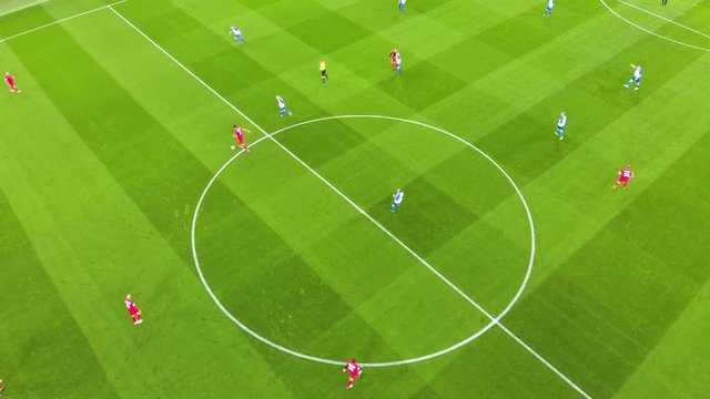 Aerial view of football players at the very beginning of the match, the game starting kick-off. On the field, one team is in red, the other is in blue and the referee is in yellow. Taken by drone