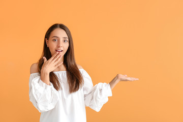 Surprised young woman showing something on color background