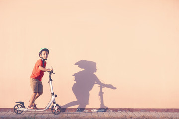 A boy in a red T-shirt riding a white scooter. The child rides a scooter. Toned Image.